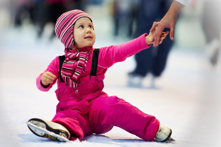Pikkulapsi opettelee luistelemaan aikuisen avulla.