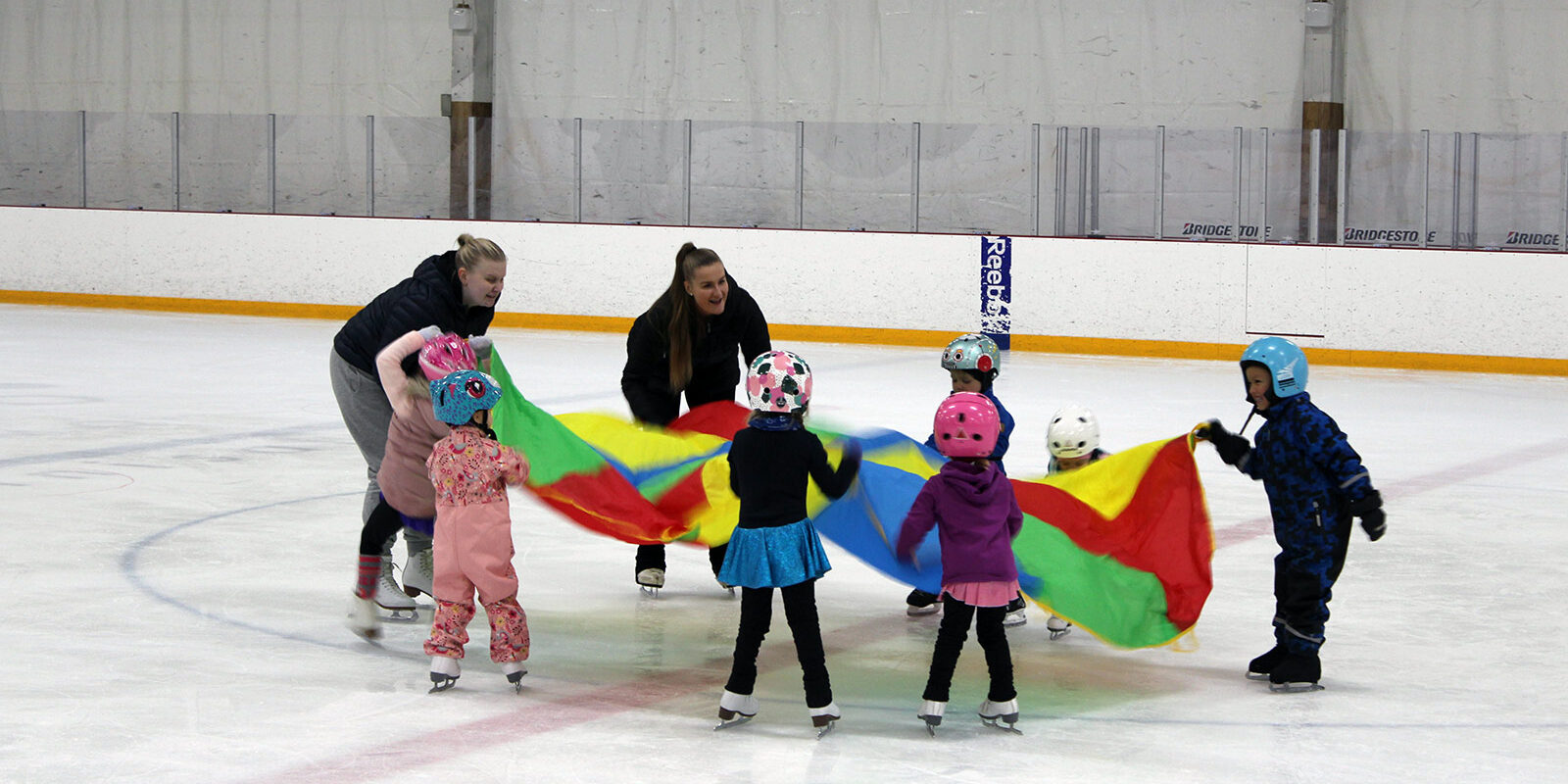 luikkakoulu_myllypuro_varjoleikki Luistelukouluohjaajat ja lapset leikkivät varjolla luistelukoululussa Myllypurossa.