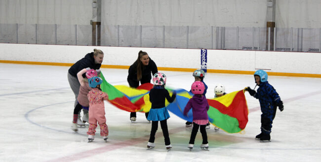 Luistelukouluohjaajat ja lapset leikkivät varjolla luistelukoululussa Myllypurossa.