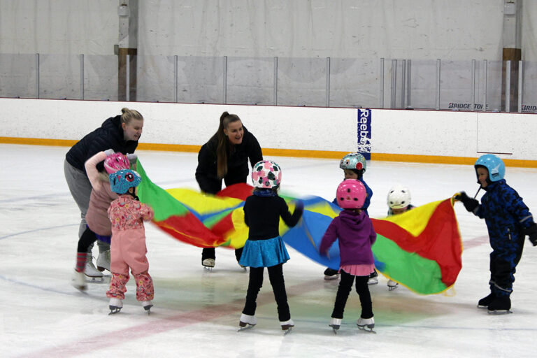 Luistelukouluohjaajat ja lapset leikkivät varjolla luistelukoululussa Myllypurossa.